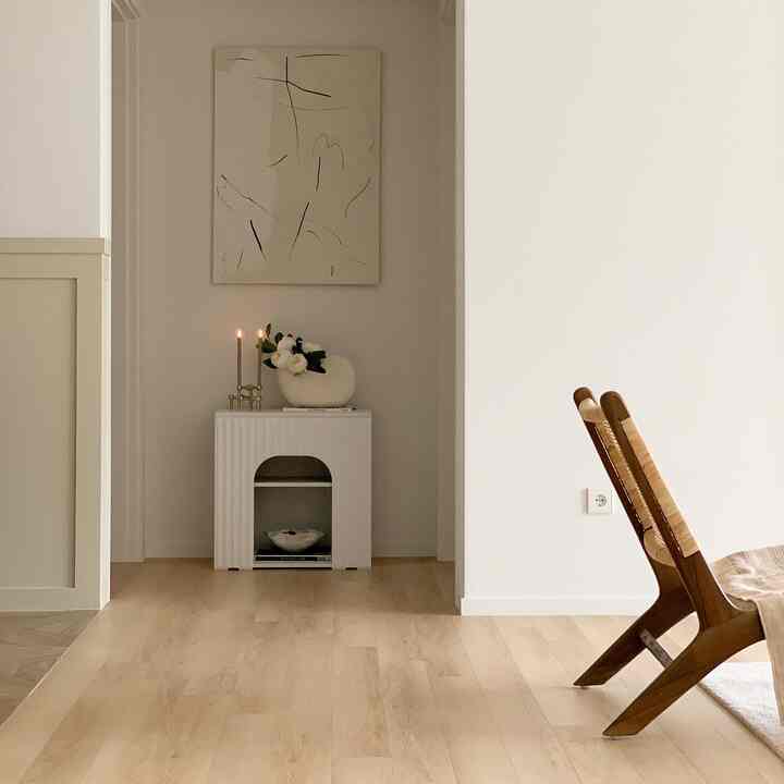 白と木目調のリビング、ミニマルで自然な印象の空間にナイトテーブルとアームチェアが配置されている