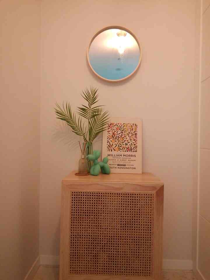 White walls and wood tone rattan cabinet with a round mirror and plant create a cozy entrance space