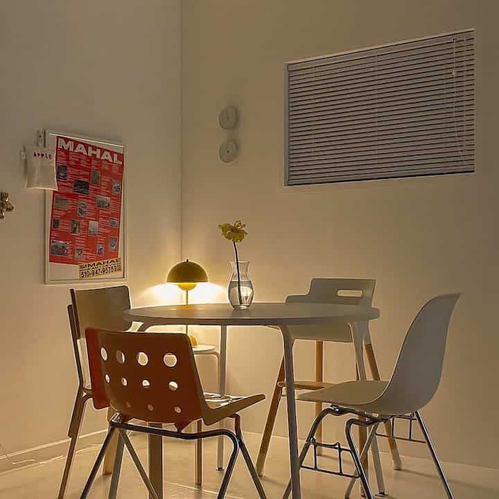 Warm-lit white tone dining room featuring round table and mix-matched chairs creating cozy and stylish atmosphere