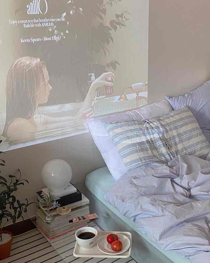 Soft blue and natural toned bedroom featuring bed with pillows and bedding, plants, and a tray with coffee creating a cozy atmosphere
