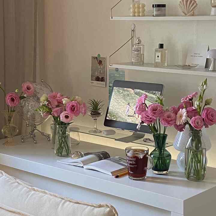 白を基調としたワンルームのホームオフィス、ピンクの花瓶と本、コーヒーカップが配置された雰囲気のある空間