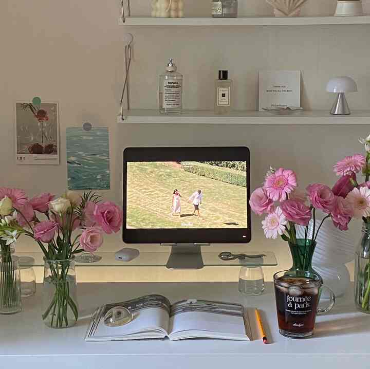 White and pink themed studio home office with a white desk featuring vases of flowers and a tablet stand for a cozy workspace