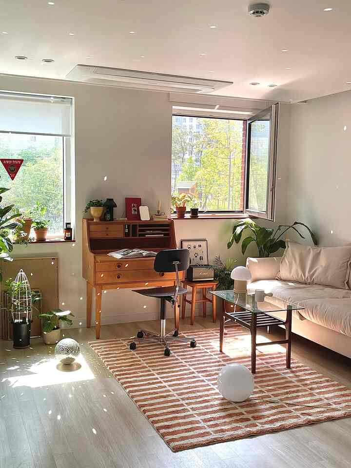 Natural brown and beige toned living room featuring sofa, coffee table, wooden desk, and plants with warm atmosphere