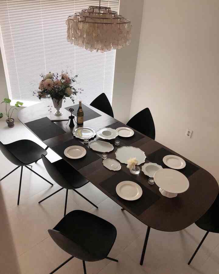 Modern dining room with white walls and ceiling, dark brown dining table surrounded by black chairs, featuring floral vase and table setting for a home party