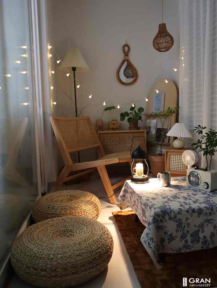 暖かいベージュと木目調のベランダ、ラタンのラウンジチェアと低いテーブル、キャンドル照明が配された雰囲気あるホームキャンプ空間