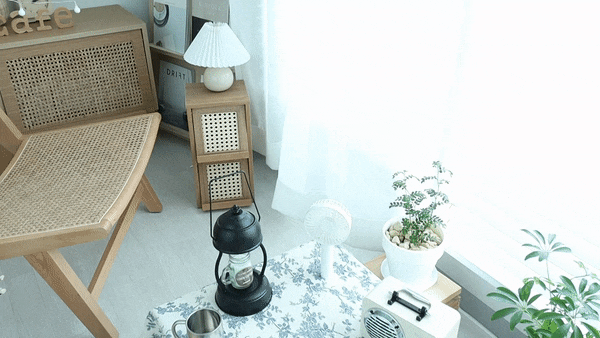 Bright and cozy living room with white and natural wood tones featuring a rattan chair, side table, and plants