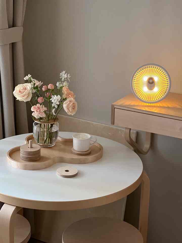 A simple, warm space featuring a white round table with natural wood tones, vase with flowers, and a candle