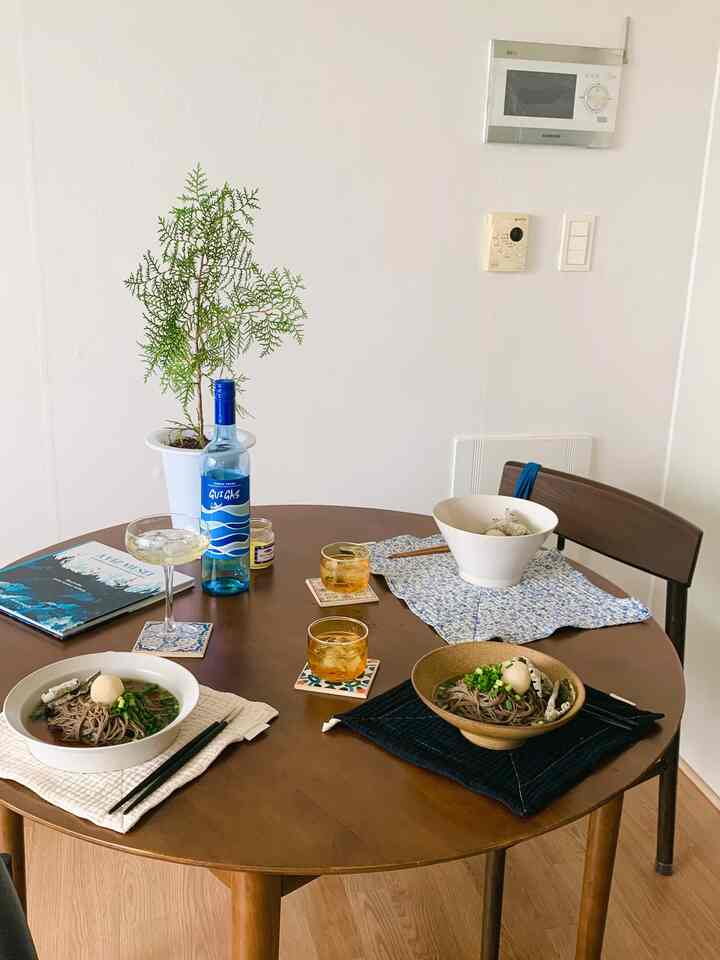 Natural wood tone dining room with white walls, round dining table set with Korean bowls and drinks, creating a warm vintage atmosphere