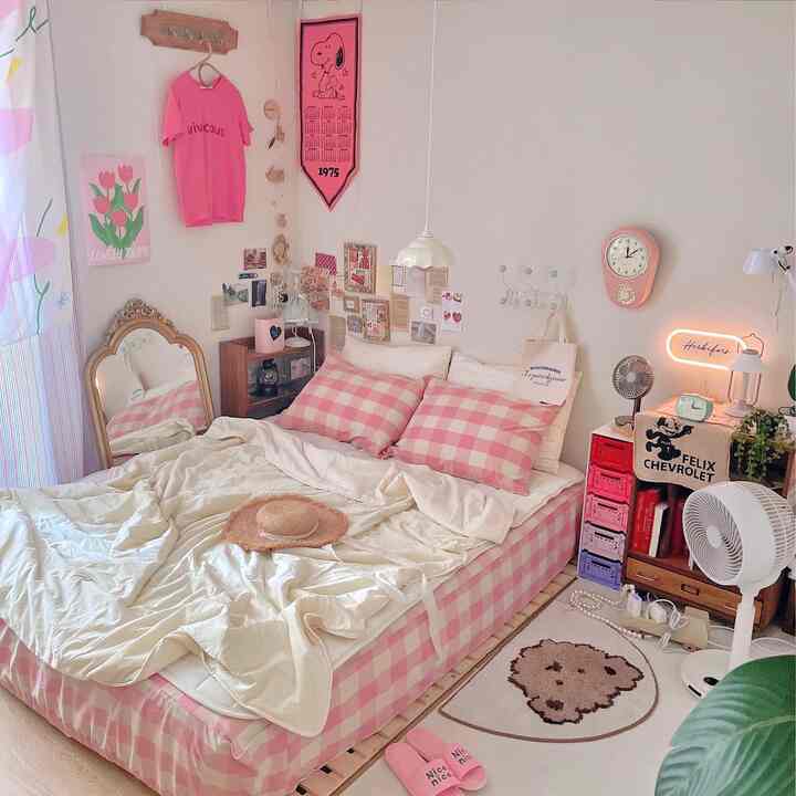 Bright bedroom with dominant pink tones featuring checkered bed and pillows, posters, clock, and rug creating cozy atmosphere