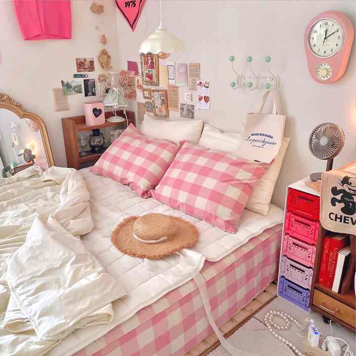 ピンクとホワイトのトーンの6畳の寝室、チェック柄の枕と収納が配置された印象的な空間