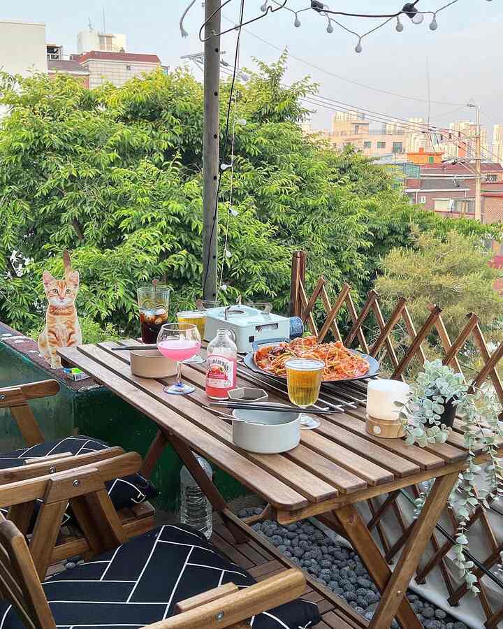 Brown wood-tone outdoor table and chairs on rooftop with lush green foliage background for home camping