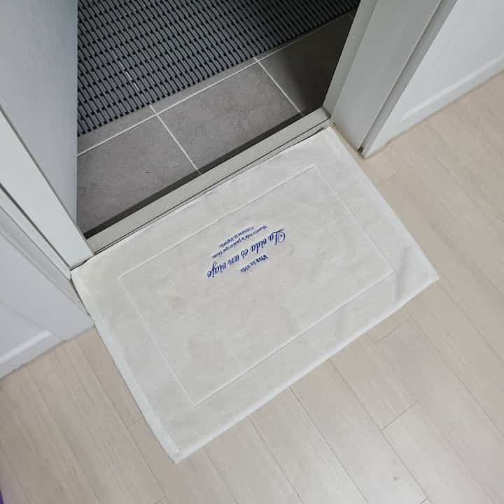 白を基調としたトイレの入口、バスマットが敷かれた清潔感のある空間