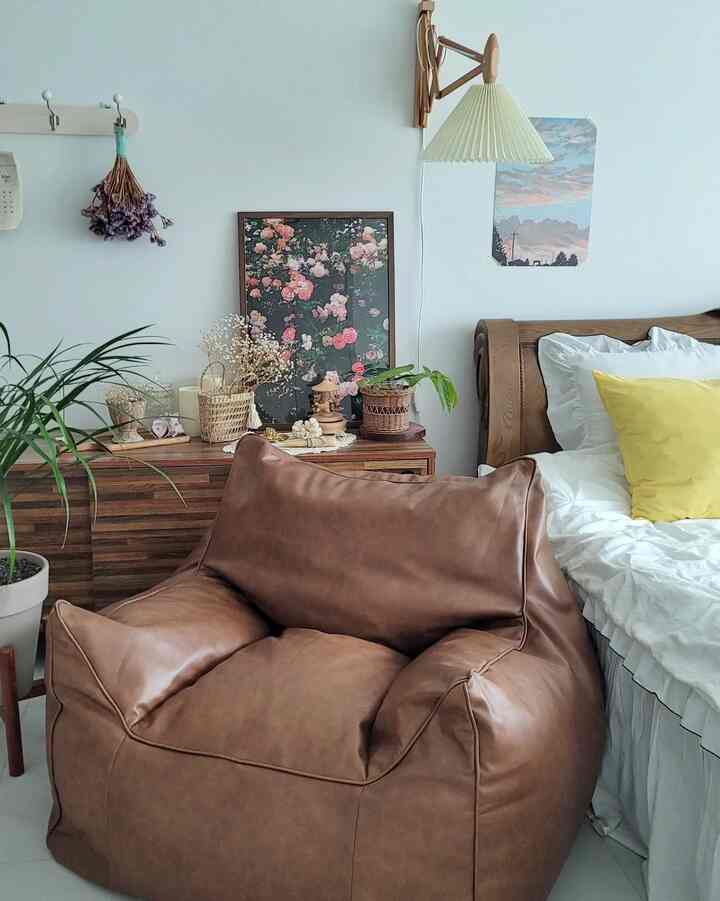 Cozy bedroom with soft brown bean bag sofa and yellow cushions on white bedding, featuring natural wood furniture and plants