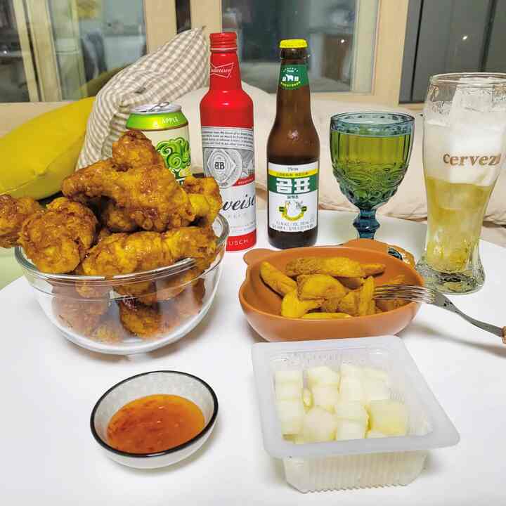 Vintage styled home bar setting with fried chicken, potato wedges, and assorted drinks on a white table, creating a cozy atmosphere