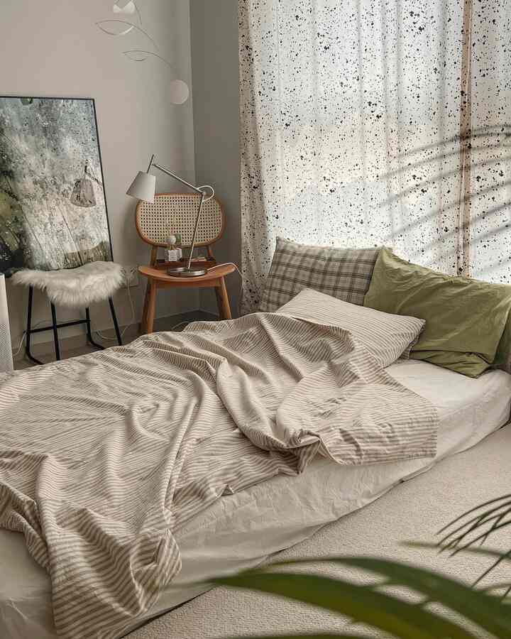 Natural color tone bedroom featuring beige striped duvet cover, rattan chair, and white sheer curtains with a cozy atmosphere