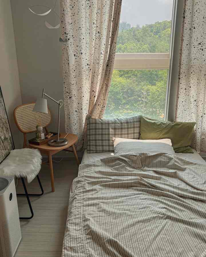 Small bedroom with natural colors and wood tones featuring a bed by the window with curtains, wooden chair, and side table creating a cozy atmosphere