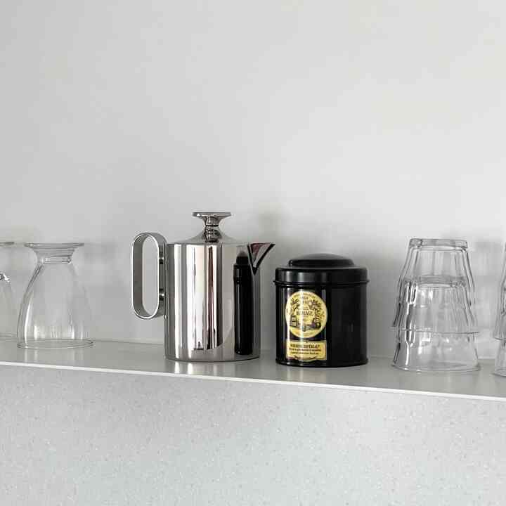 Clean kitchen space with white walls and shelf holding a stainless steel teapot, black tea canister, and clear glass cups