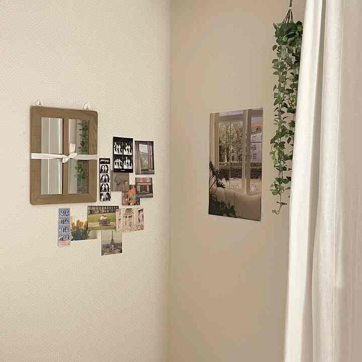 白とベージュのトーンが調和するコーナー空間、額縁やポスター、植物のつるが配置された印象的なインテリア