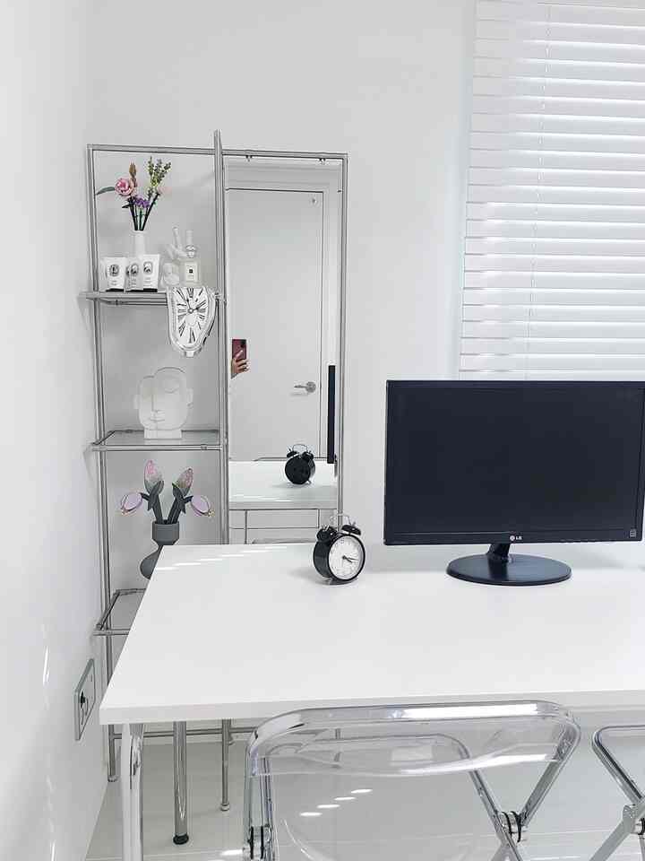 White and transparent toned home office featuring a clean desk, monitor, and alarm clocks with a minimalist atmosphere