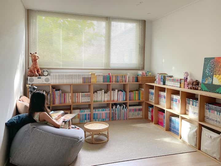 ナチュラルな木目調とベージュのラグが調和した子供部屋、本棚とビーズクッション、ラタンテーブルが配置された雰囲気のある読書スペース