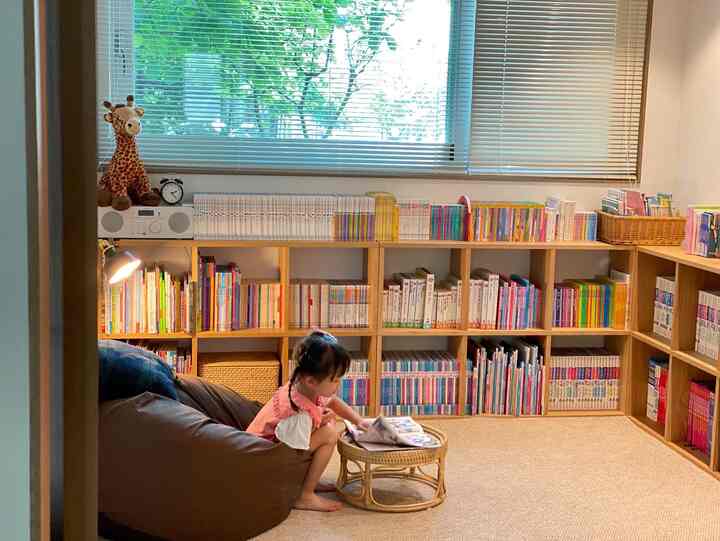 Natural-toned kids' room featuring large bookshelves and a rattan stool with a child reading peacefully