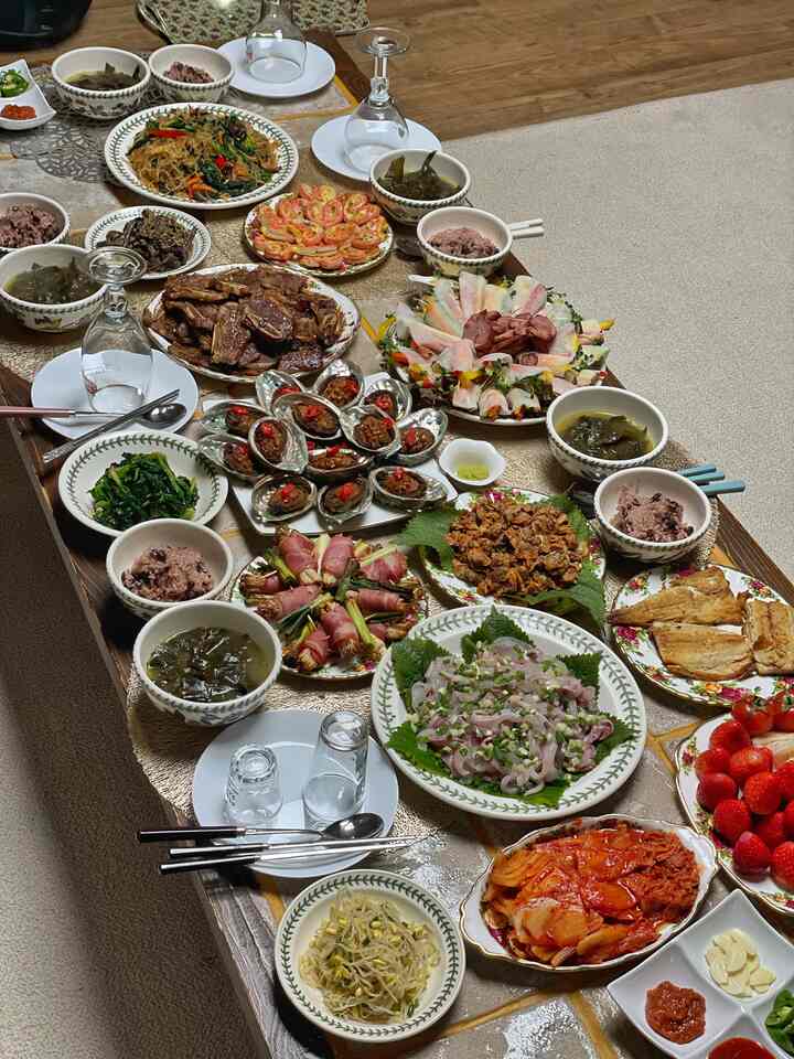 ナチュラルな色調のキッチンスペース、広い木製のダイニングテーブルに伝統的な韓国料理が並び、雰囲気のあるホームパーティーインテリア