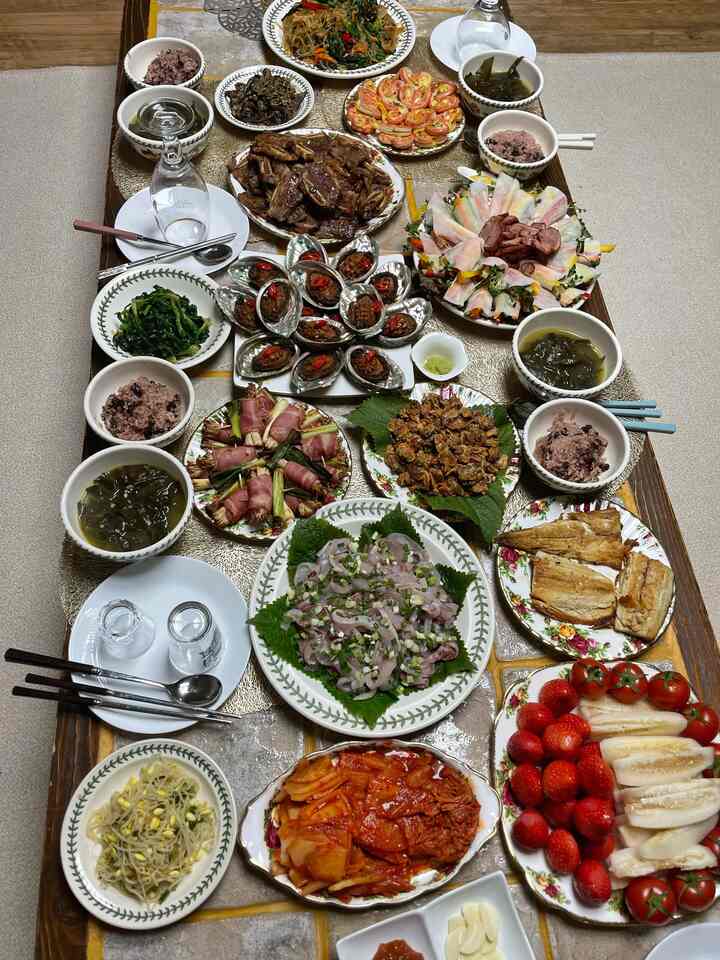 暖かい木目調のダイニングテーブルに、4人暮らし向けの多彩な韓国の副菜と皿が豊かに並べられた食卓