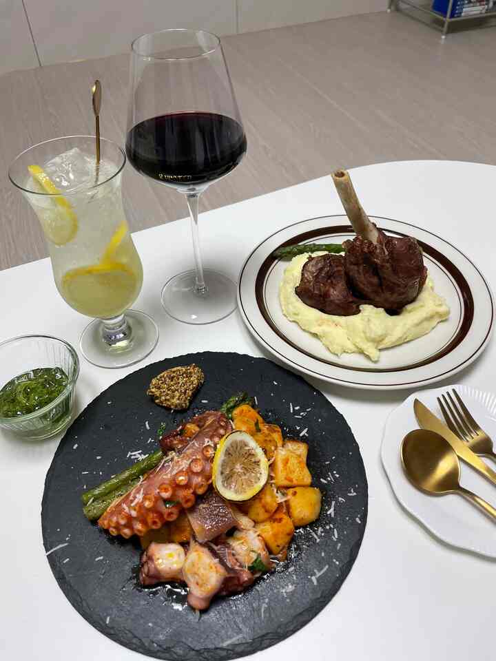 ホワイトとグレイのトーンのダイニング、石のようなプレートと高級感のある料理、ワイングラスが配置された印象的な空間