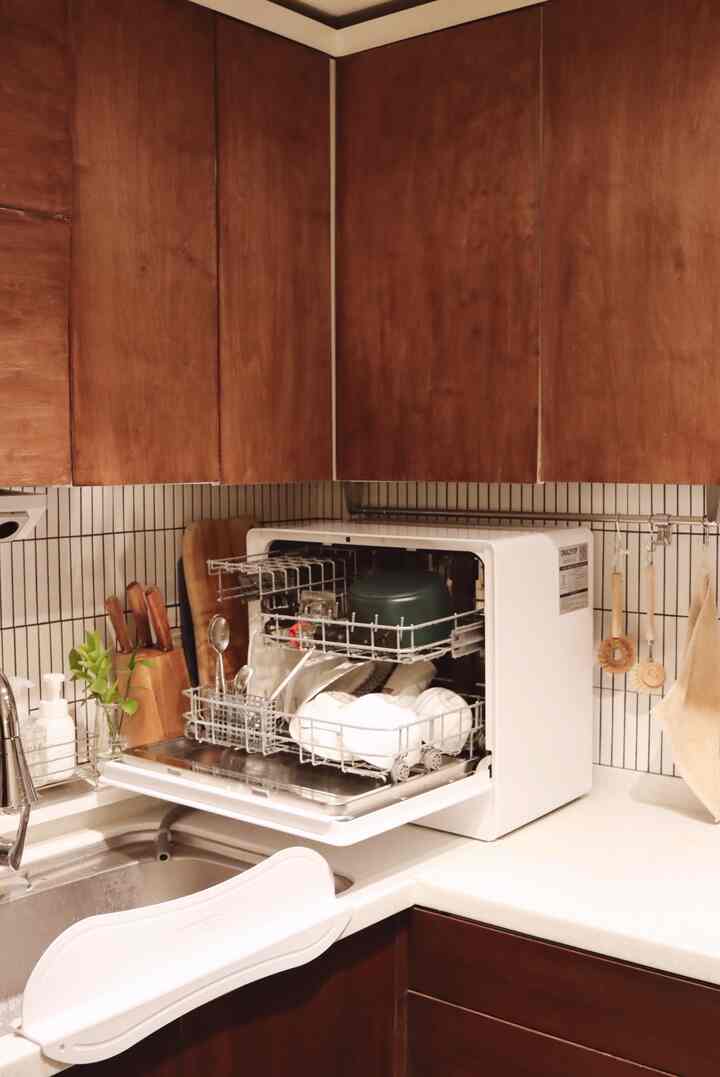 Kitchen space with brown wood cabinetry and a white dishwasher, featuring cutting boards and kitchen utensils arranged neatly, creating a clean atmosphere