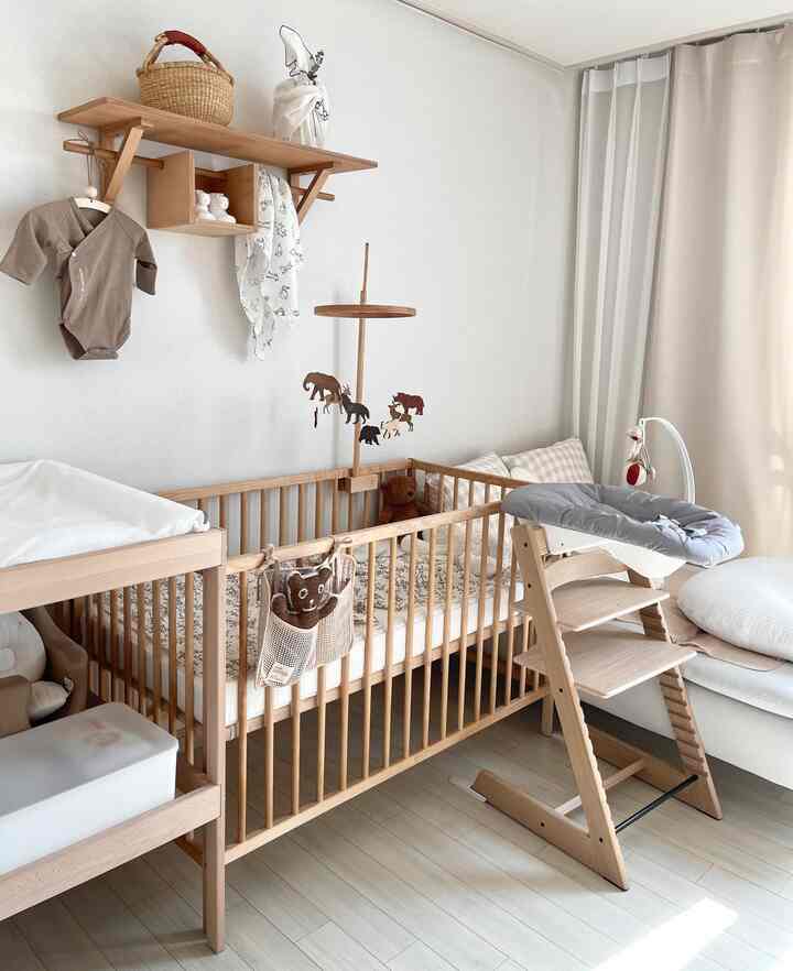 ナチュラルな木目調が調和した子供部屋、ベビーベッドとおむつ交換台、白いカーテンが配置された温かく落ち着いた雰囲気のインテリア