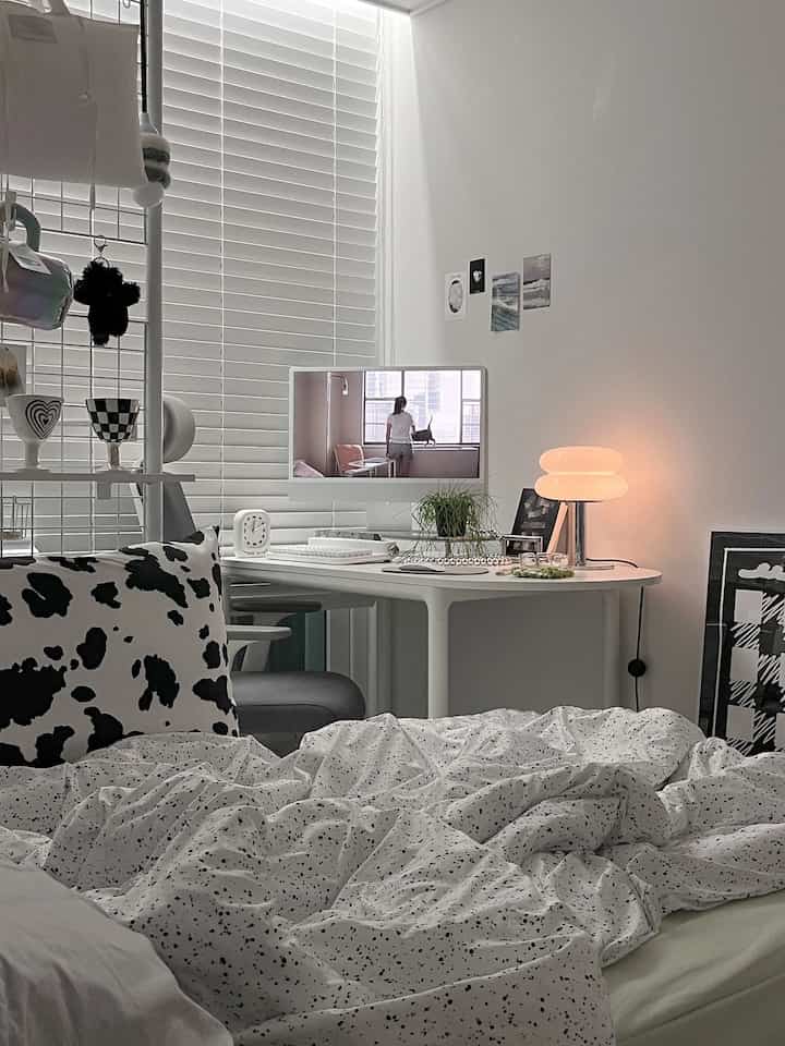 White tone bedroom space featuring an oval desk with computer and cozy bedding in a modern, simple atmosphere