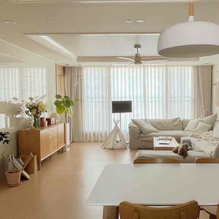 White and wood-toned living room featuring a large sectional sofa, curtains, and a dog, creating a cozy natural space