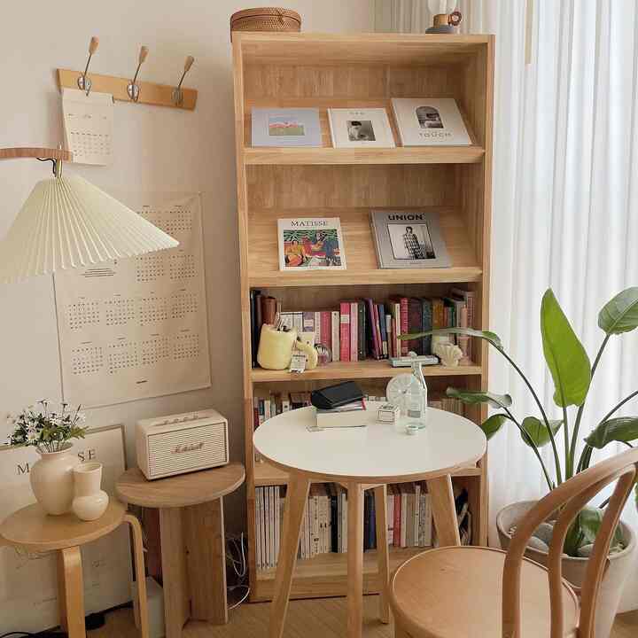 Bright white and beige-toned living room with a natural interior featuring a wooden bookshelf, round table, and large white sheer curtains