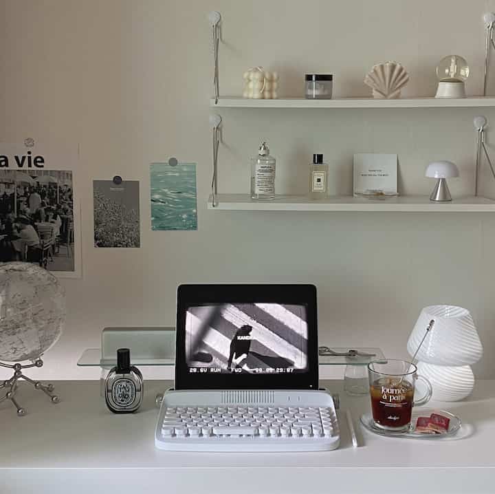 White-tone studio apartment home office featuring a clean white desk with modern lamp centrally placed, and decorative objets on shelves creating a simple workspace