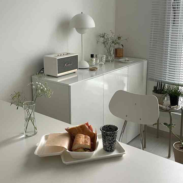 ホワイト調のワンルームリビング、シンプルな家具と収納棚が配置され、ホームカフェ風のテーブルセットがある雰囲気のあるインテリア