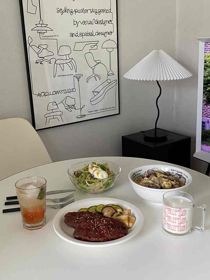 白を基調としたリビングのダイニングスペース、丸いダイニングテーブルと大きな額縁ポスター、個性的なフロアランプが配置されたシンプルモダンな雰囲気のインテリア