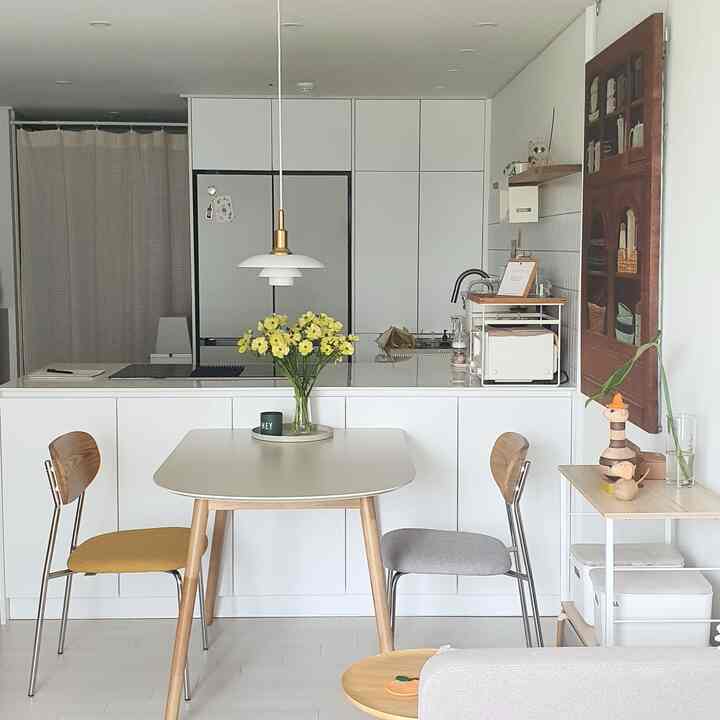 白と木目調が調和したキッチン空間、ダイニングテーブル上の黄色い花瓶が配置されたモダンでシンプルな雰囲気のインテリア