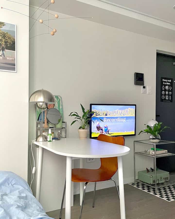 White and blue toned studio apartment featuring a white oval table with orange chair centrally, minimal modern interior