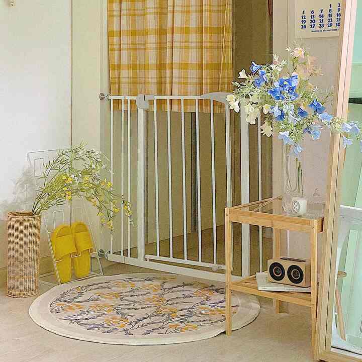 White and yellow-toned entrance featuring a safety gate, rattan vase, blue and white flowers, and a circular floral rug with cozy atmosphere