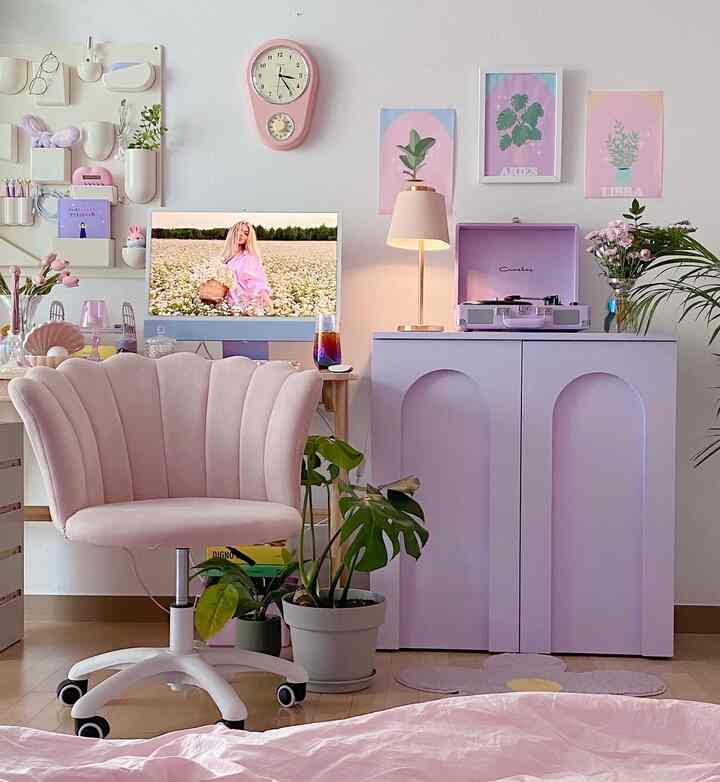A pink and lavender-toned home office featuring a pink velvet chair, iMac, and a lilac storage cabinet with cozy decor accents