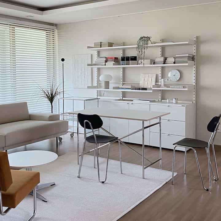 Bright and natural white and wood-toned living room and home office space featuring modular furniture and organized bookshelves with a clean aesthetic