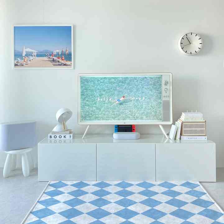 White and blue toned living room featuring a TV stand with decor items and wall clock, blue diamond pattern rug on the floor, creating a clean atmosphere