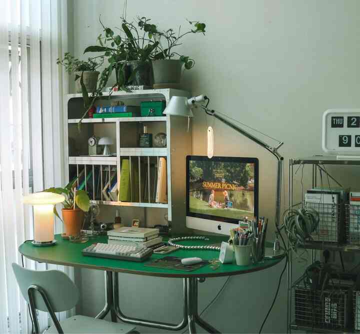 Green-toned home office space featuring a desk, bookshelf, shelves, and lighting creating a clean work environment