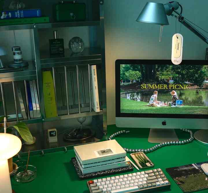 グリーンのトーンが特徴のホームオフィス、机にはコンピューターとノート、シルバーの金属製本棚が配置されたモダンなインテリア