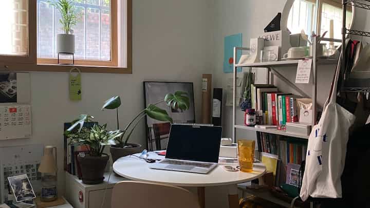 白と木目調の小さなホームオフィス、丸テーブルと本棚が配置された落ち着いた在宅勤務空間