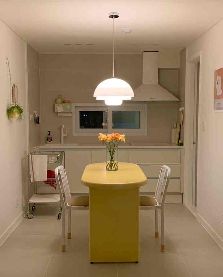 黄色のダイニングテーブルと白い椅子が配置された清潔なキッチンとダイニングルーム、中央に花瓶と花が置かれた温かみのある空間