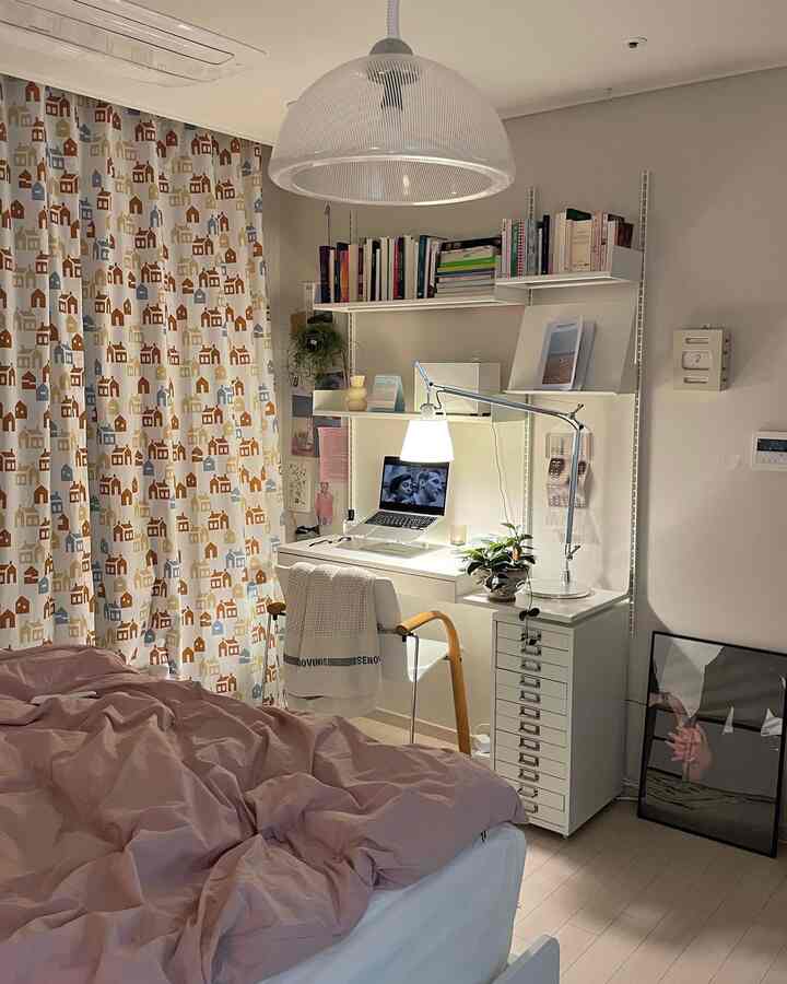 A white and pink toned bedroom featuring a desk and shelves, creating a simple and cozy home office integrated space