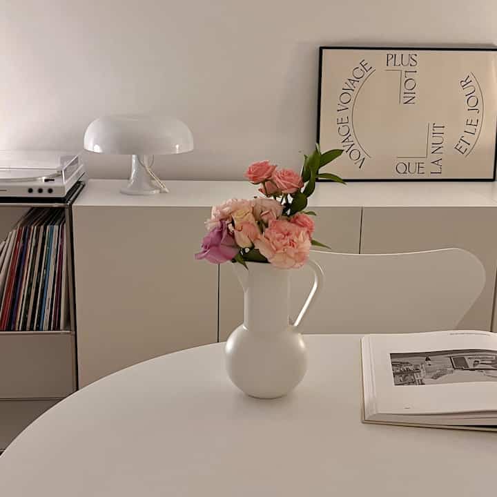 Bright white-toned interior space featuring a simple modern design with a white vase holding coral-colored flowers centrally placed