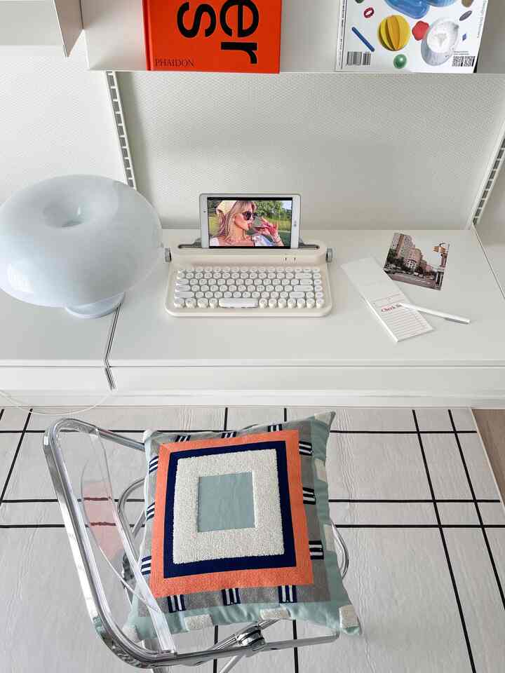 白を基調としたコンパクトなホームオフィス、透明なアクリルチェアに北欧柄のクッションとレトロなキーボードが置かれた整ったデスク