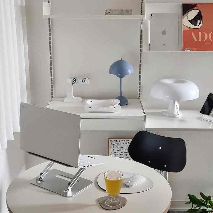 A white-dominant home office space featuring modern desks and a black office chair, accented by blue and white lamps as focal points.